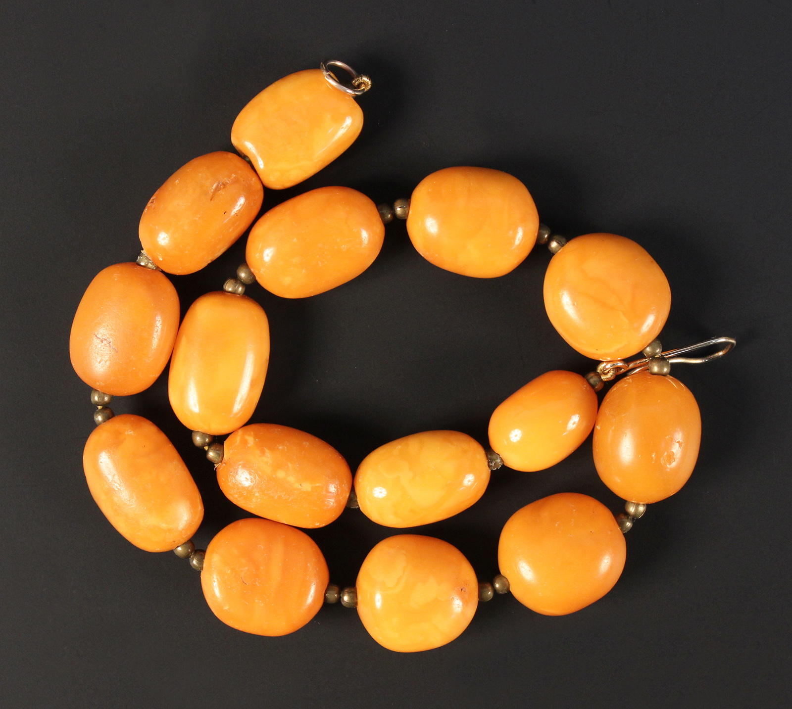 A single row necklace of fifteen mottled honey coloured opaque