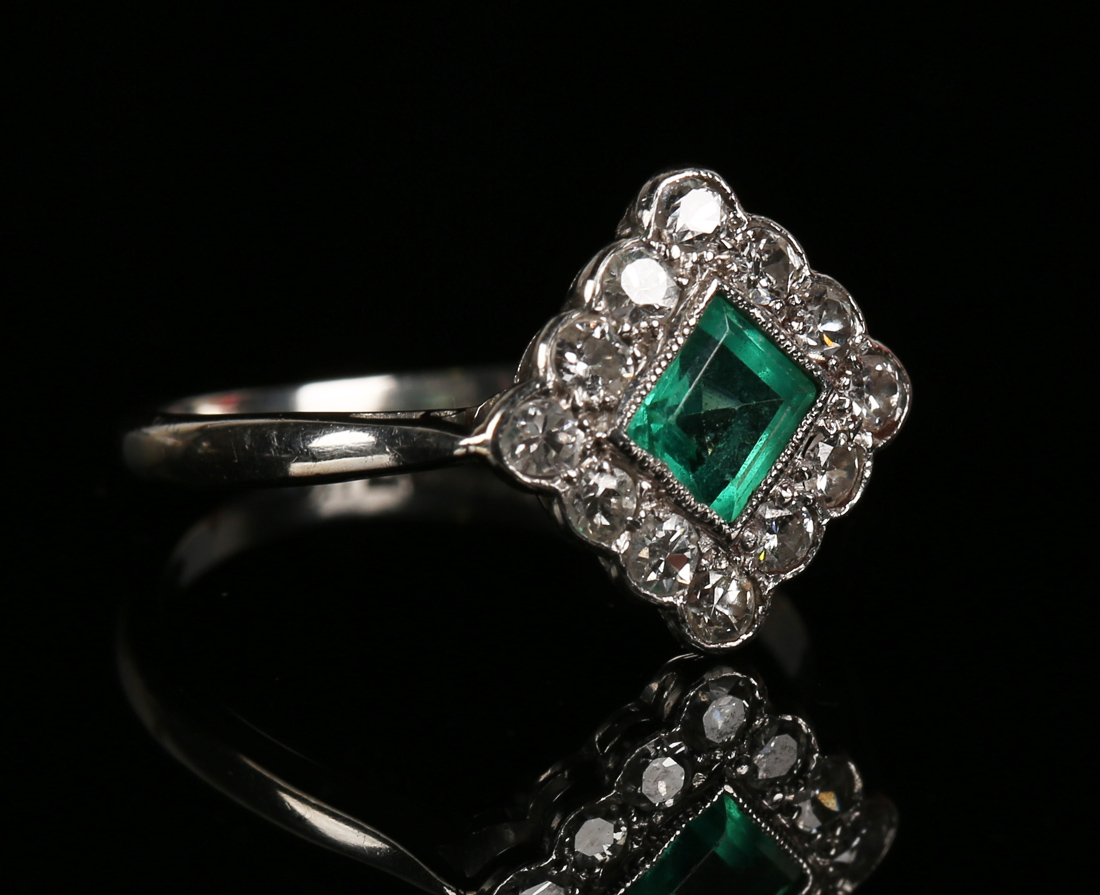 A platinum, emerald and diamond lozenge shaped cluster ring, mounted ...