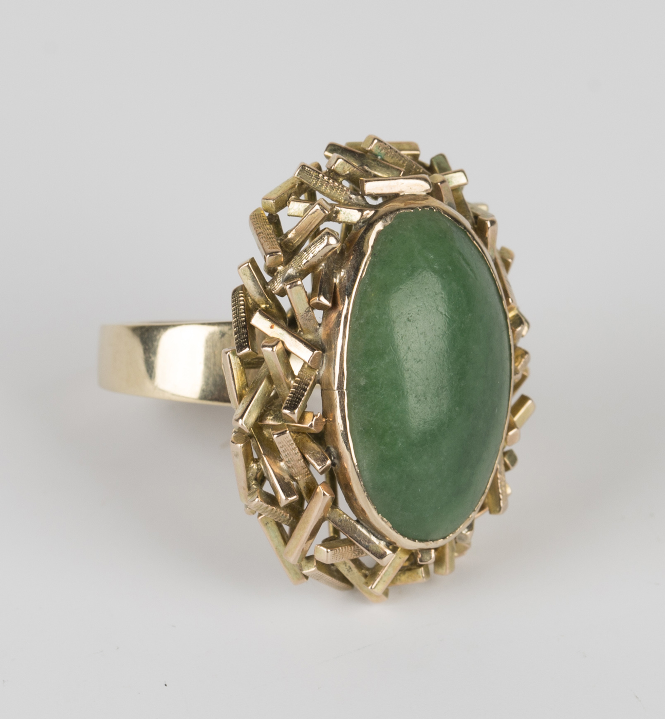 A gold ring, mounted with an oval jade within an abstract surround ...