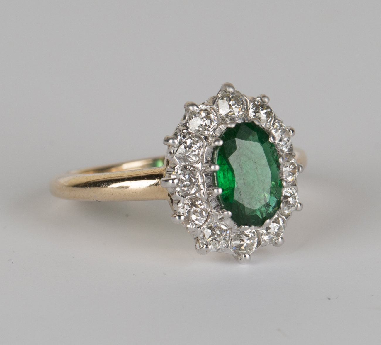 A gold, emerald and diamond oval cluster ring, claw set with the oval ...