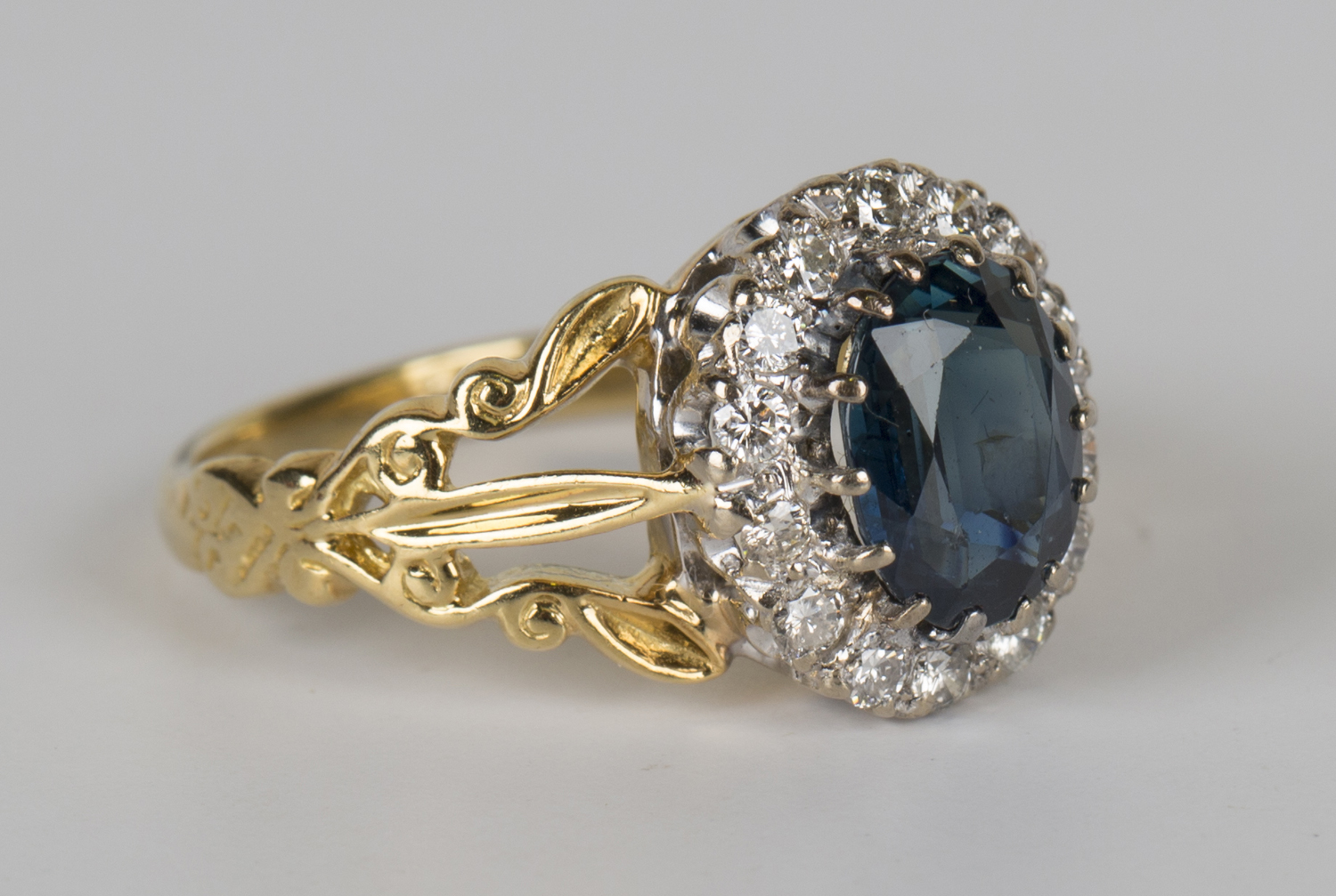 An 18ct gold, sapphire and diamond oval cluster ring, claw set with the ...