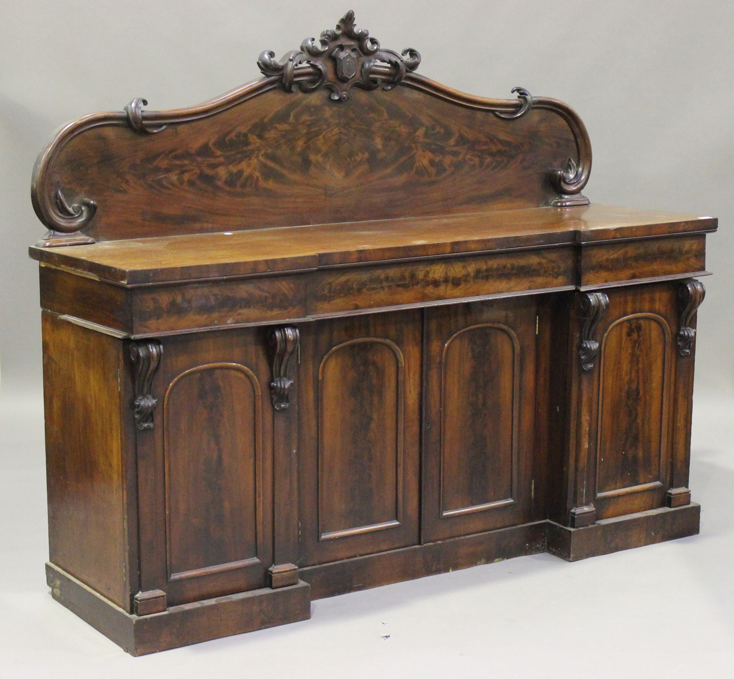 A Victorian mahogany sideboard, the arched back with a carved surmount ...