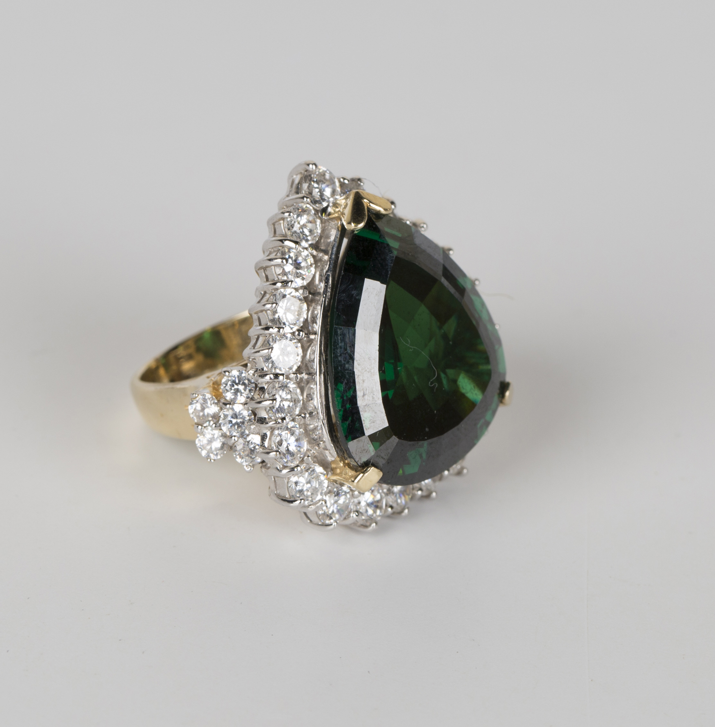 A gold, green and colourless gem set ring in a drop shaped design ...