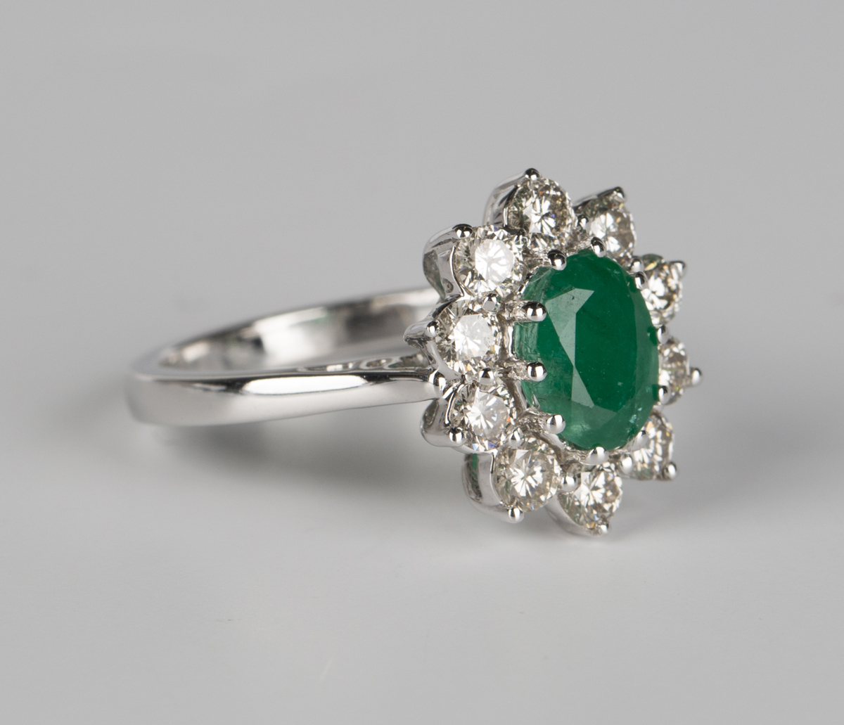 A white gold, emerald and diamond cluster ring, claw set with an oval ...