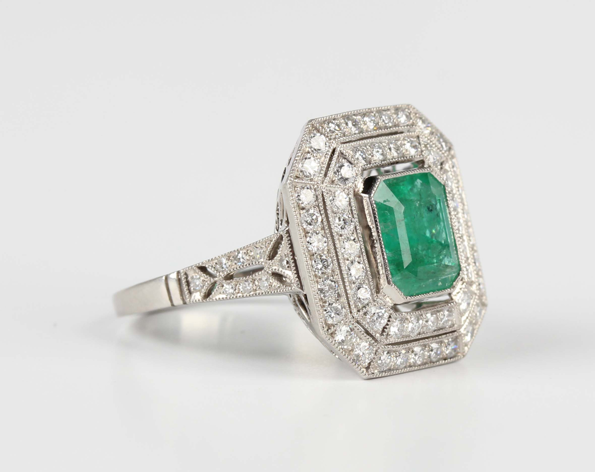 A platinum, emerald and diamond cluster ring, collet set with a cut ...